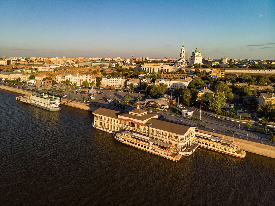 Luftaufnahme von Ausflugsbooten und schwimmendem Restaurant entlang Promenade am Ufer von Fluss Wolga mit Astrachaner Kreml dahinter, Astrachan, Bezirk Astrachan, Russland, Europa