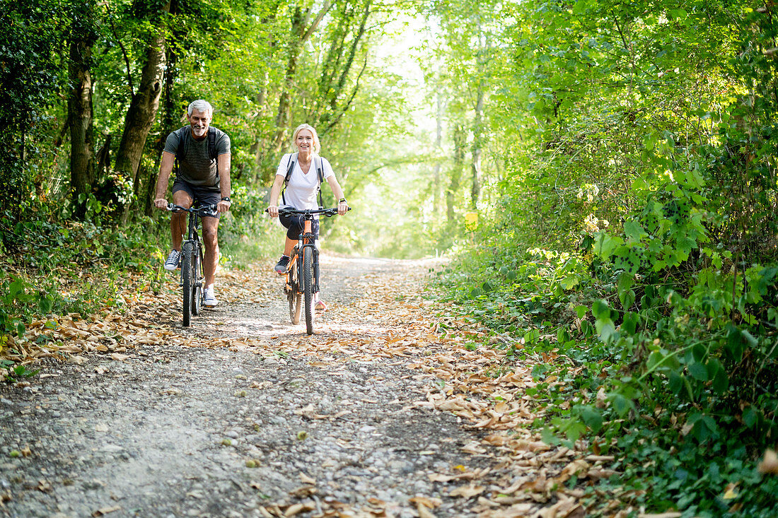 Portrait of smiling mature couple riding bicycles on footpath in forest