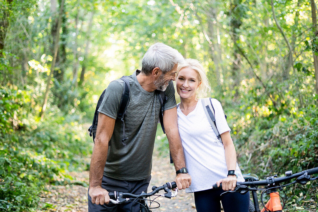Smiling mature couple with bicycles standing in forest