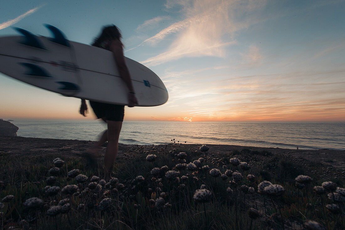 Surferin geht zum Sonnenaufgang zum Meer, Portugal