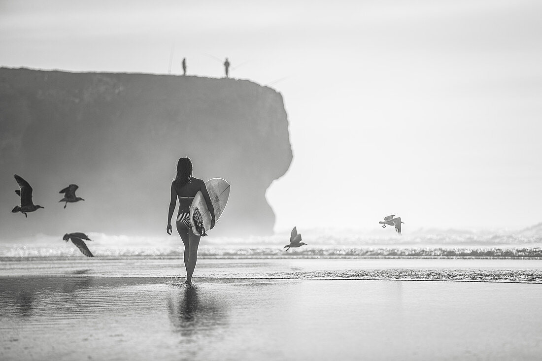 Surferin geht am Strand von Portugal mit ihrem Surfbrett