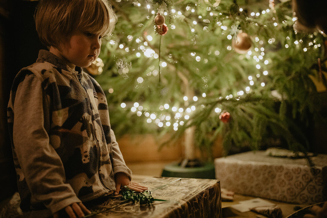 Kleiner Junge packt vorm Christbaum seine Geschenke aus