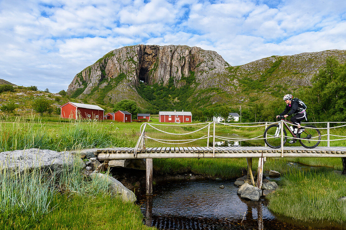 Cyclists on small bridge with red houses in front of Torghattan, Bronnoysund, Norway