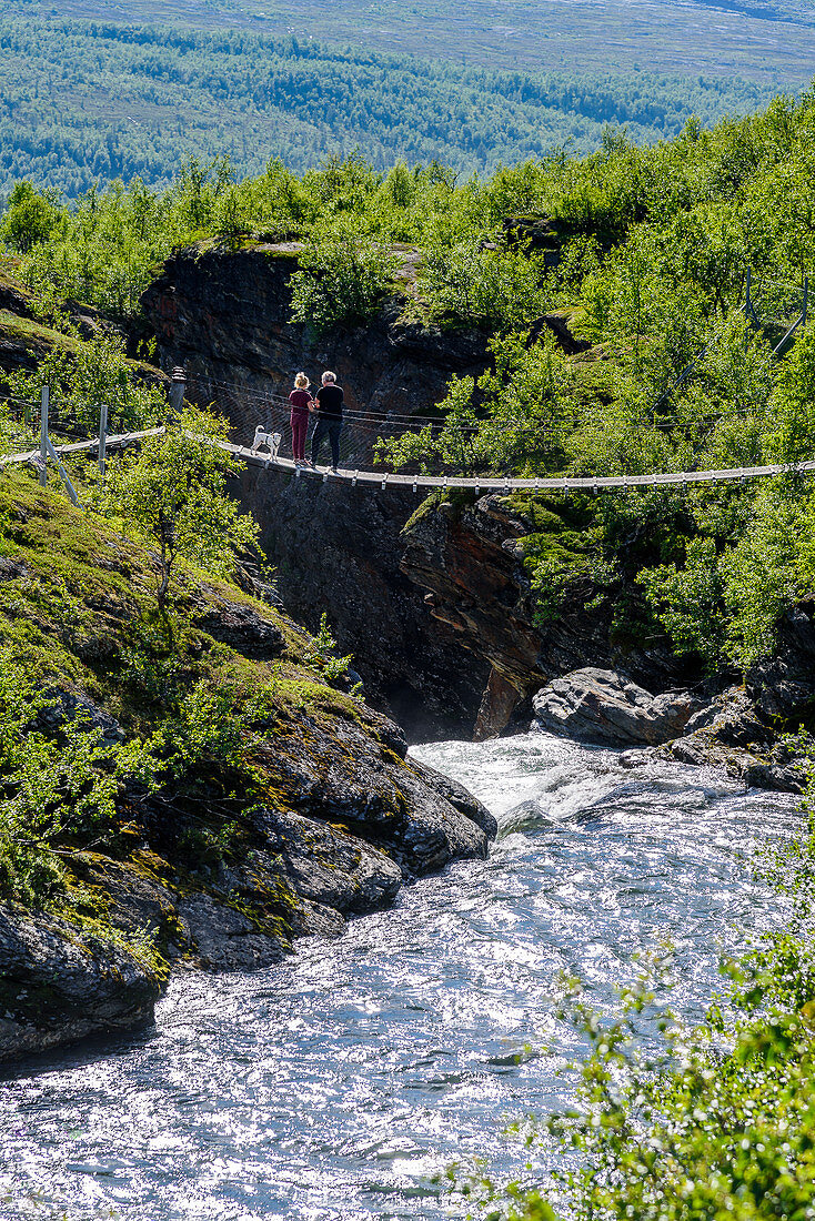Suspension bridge with people, mountain panoramas and gorges along the Silvervägen (R 77) to Junkerdal, Norway
