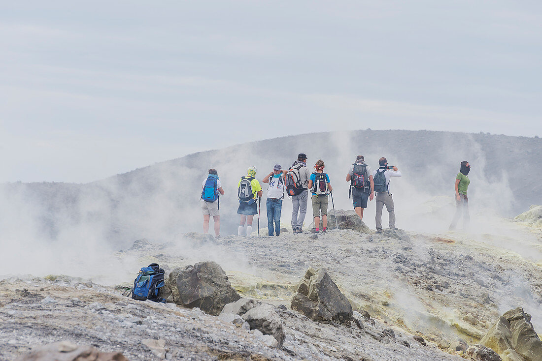 Hikers walking through fumaroles smoke on Gran Cratere rim, Vulcano Island, Aeolian Islands,  Sicily, Italy, 