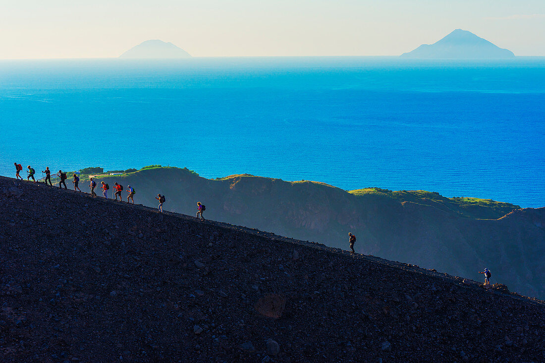 Hikers walking around Gran Crater rim, Vulcano Island, Aeolian Islands, Sicily, Italy