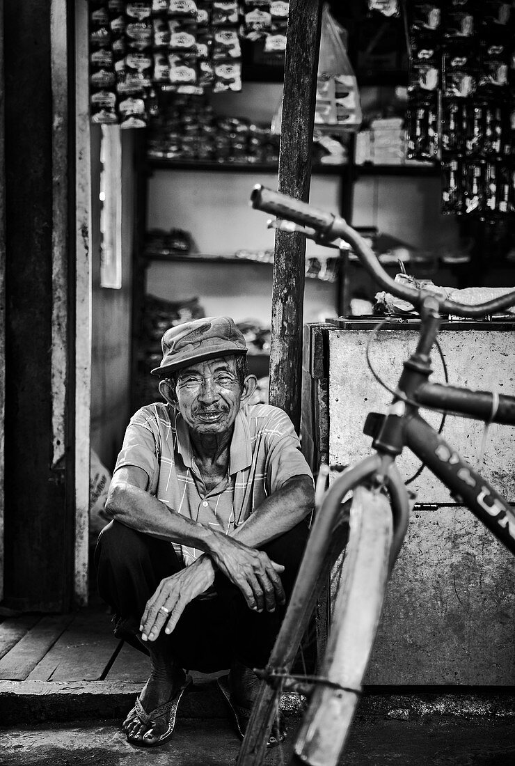 Ein indonesischer Ältester sitzt in der Tür seines Ladens auf einem Markt in Palangkaraya, Zentral-Kalimantan, Borneo, Indonesien