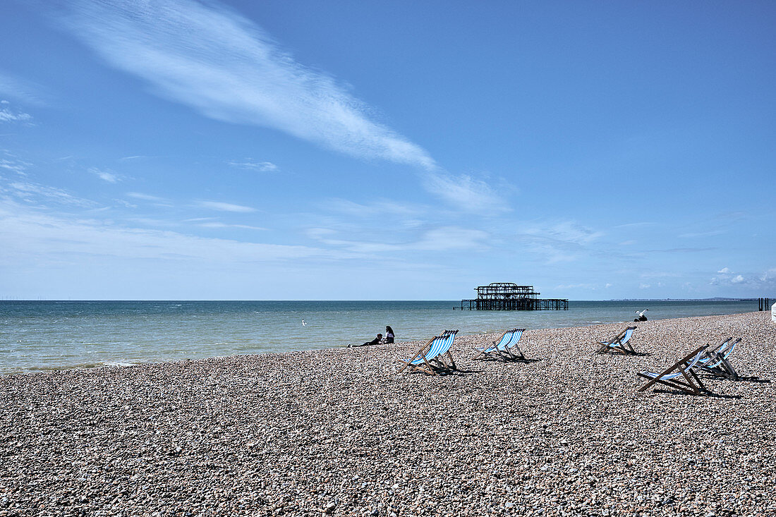 Brighton Beach with people and deck chairs on a spring day, Brighton, East Sussex, UK.