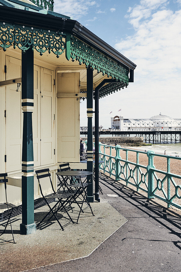Tables and chairs at the seaside on Brighton Beach, looking through to the Brighton Palace Pier, East Sussex, UK.
