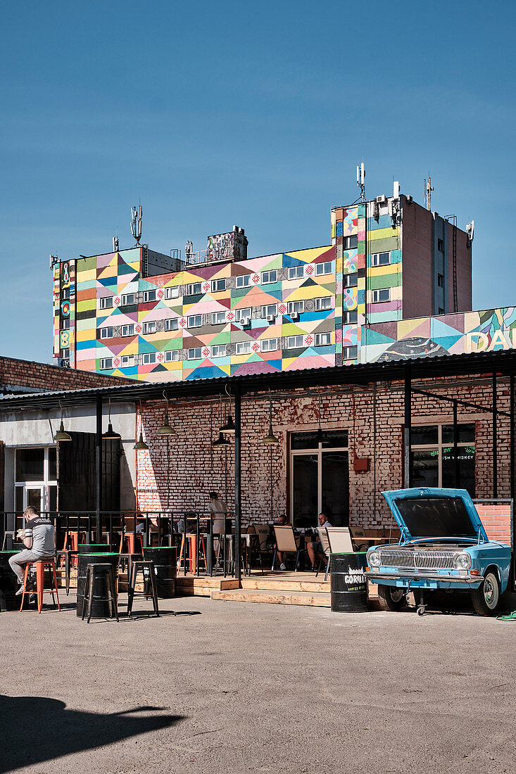 Ein Innenhof mit Bars im Hipster Leninsky Viertel in der Nähe der Oktyabrskaya-Straße mit einem bunt bemalten Wohnhaus im Hintergrund, Minsk, Belarus