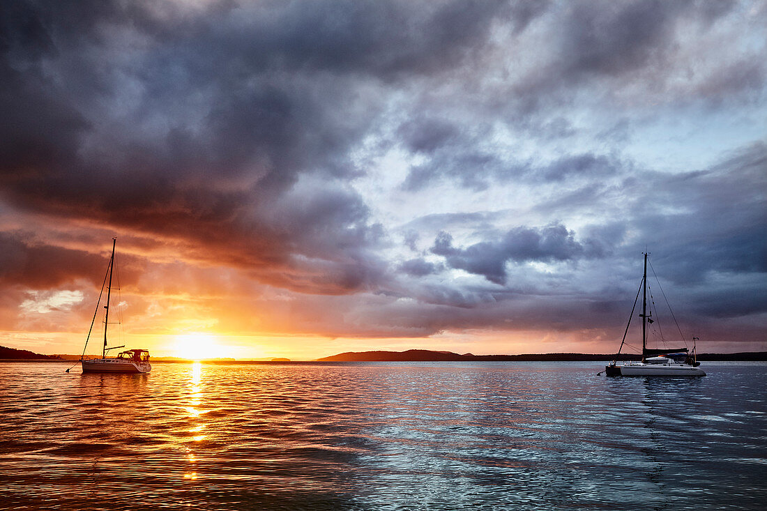 Goldene Stunde bei Sonnenuntergang in der Nelson Bay, New South Wales Australien, während ein Sturm über die auf dem Wasser vertäuten Boote hinwegzieht