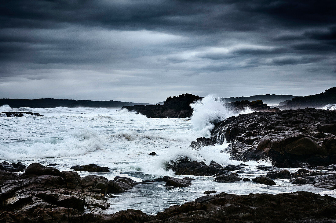 Wellen brechen auf Felsen an einem dunklen stürmischen Tag im Herbst im Tomaree National Park, Nelson Bay, New South Wales, Australien