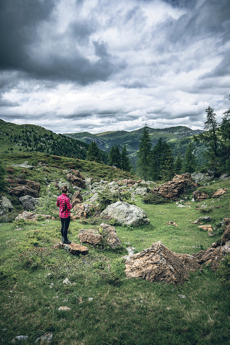 Woman stands on a rock and takes cell phone pictures of the red rocks at the red castle, Nockberge Biosphere Park, Carinthia, Austria, Europe.