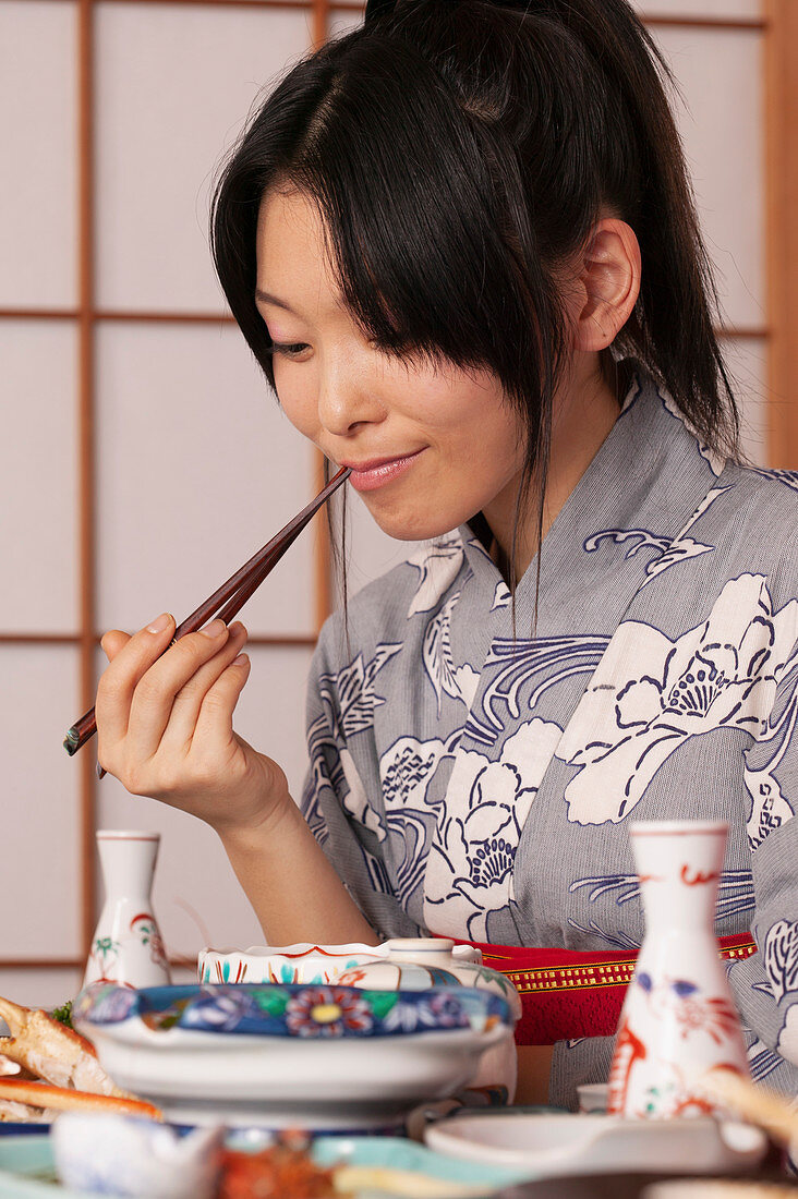 Junge Frau im Kimono, die traditionelles japanisches Essen mit Stäbchen isst