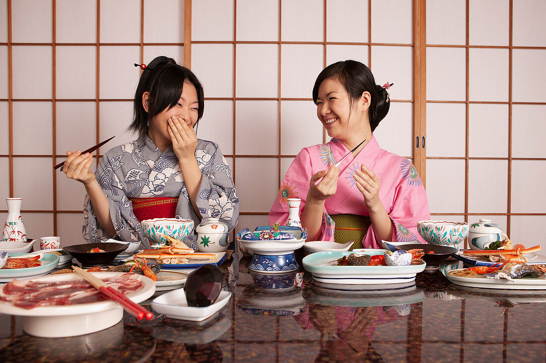 Happy young women in kimonos eating dinner in restaurant