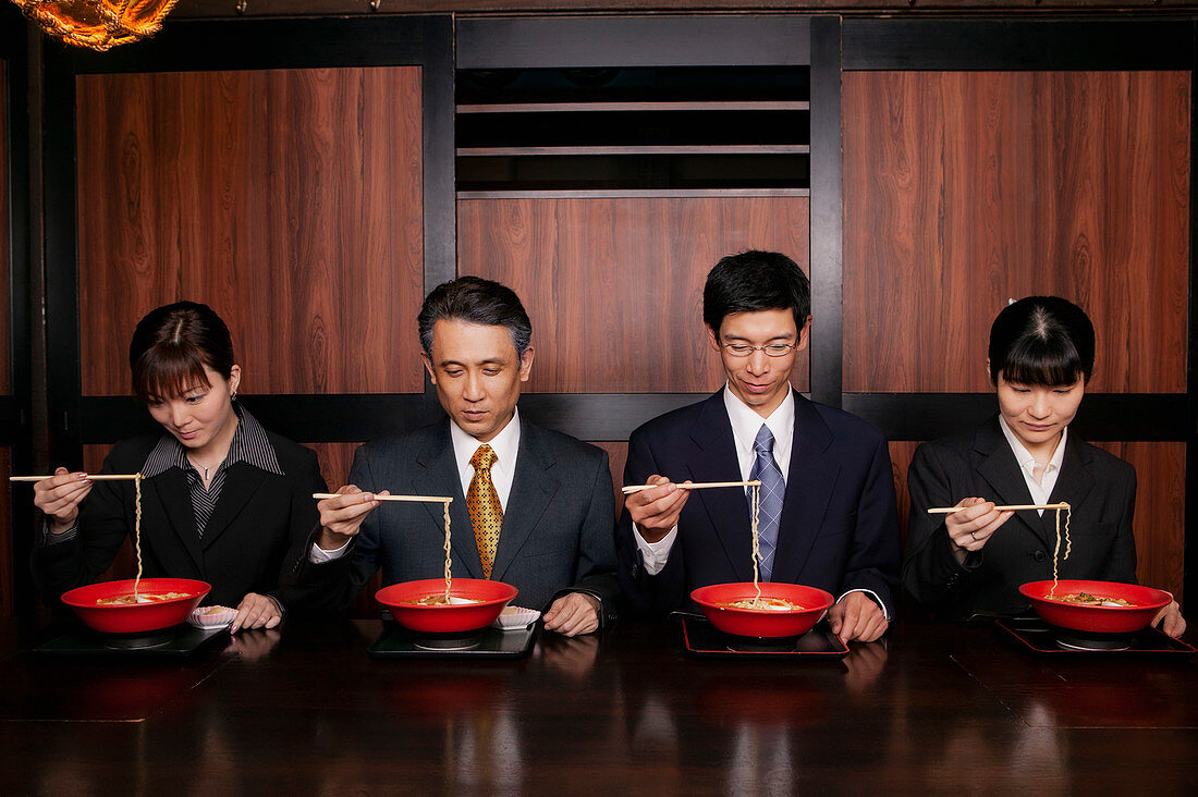 Japanese business people in suits eating ramen with chopsticks in restaurant