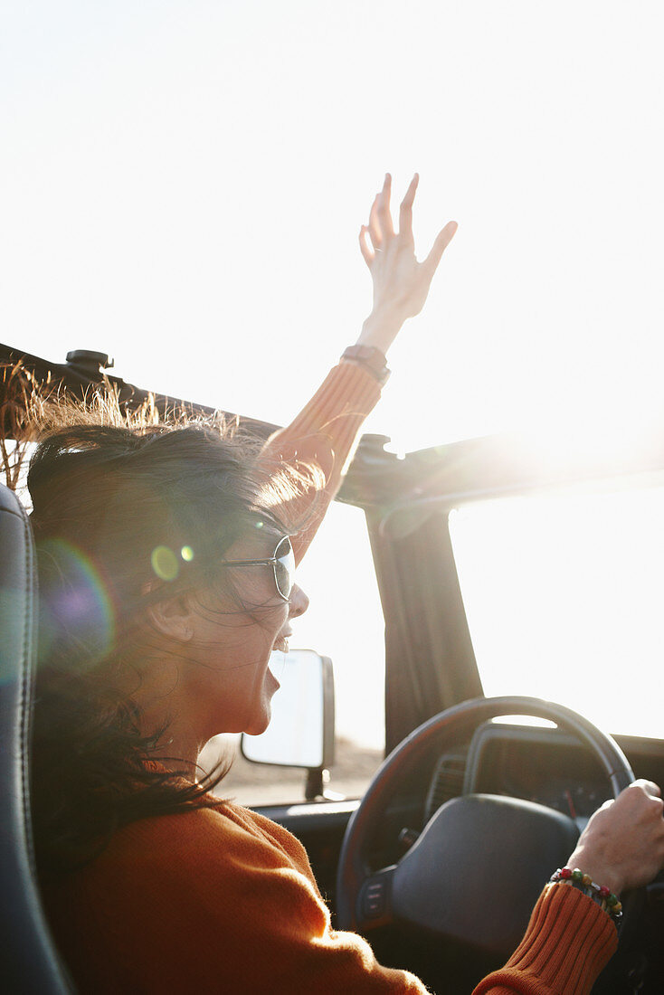 Hispanic woman raising arms while driving