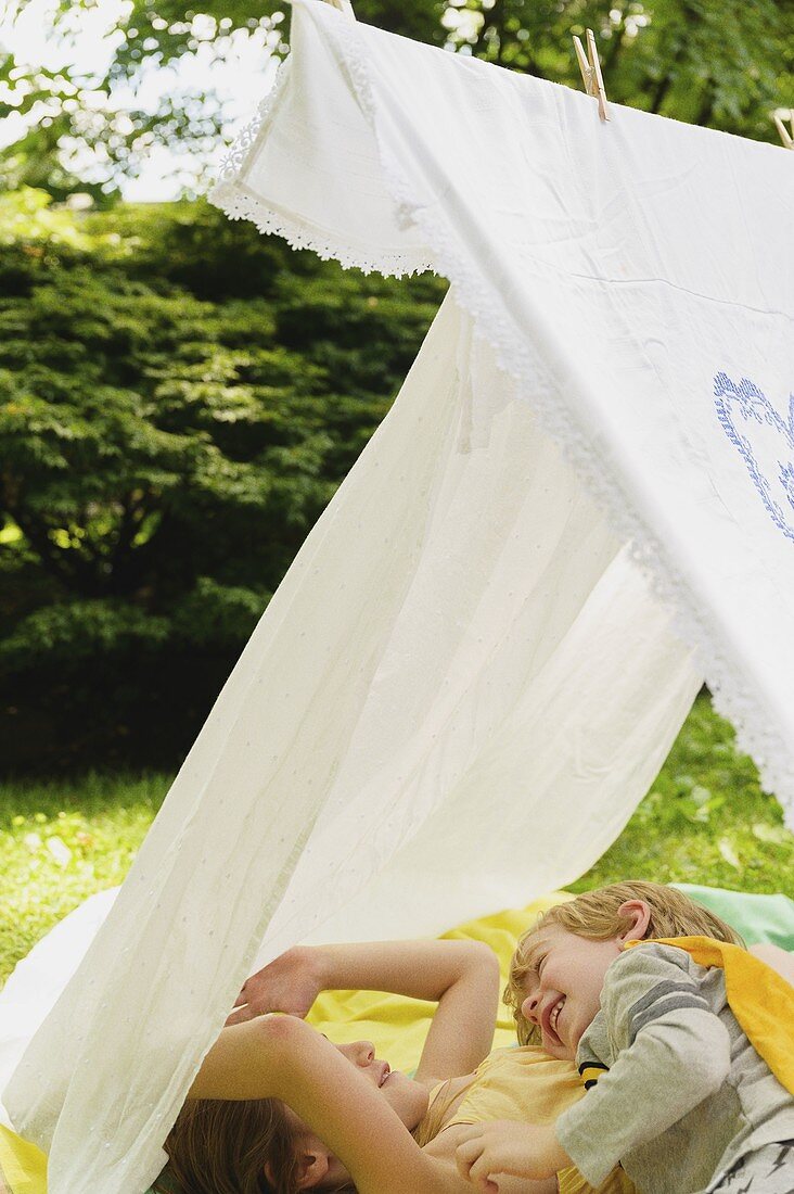 Mädchen (6-7 Jahre) und Junge (4-5 Jahre) entspannen im selbstgebauten Zelt im Hinterhof
