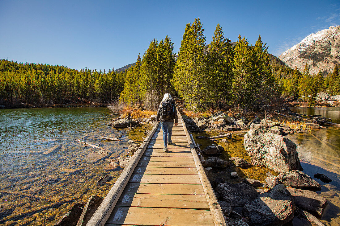 USA,Wyoming,Jackson,Grand Teton National Park,Senior woman walking on wooden path over Taggart Lake in Grand Teton National Park