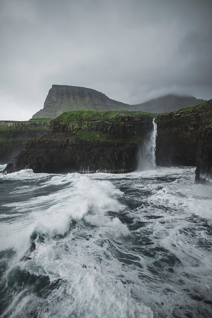 Denmark,Faroe Islands,Gasadalur Village,M?Lafossur Waterfall,Coastline with Mulafossur Waterfall falling into Atlantic Ocean in stormy day