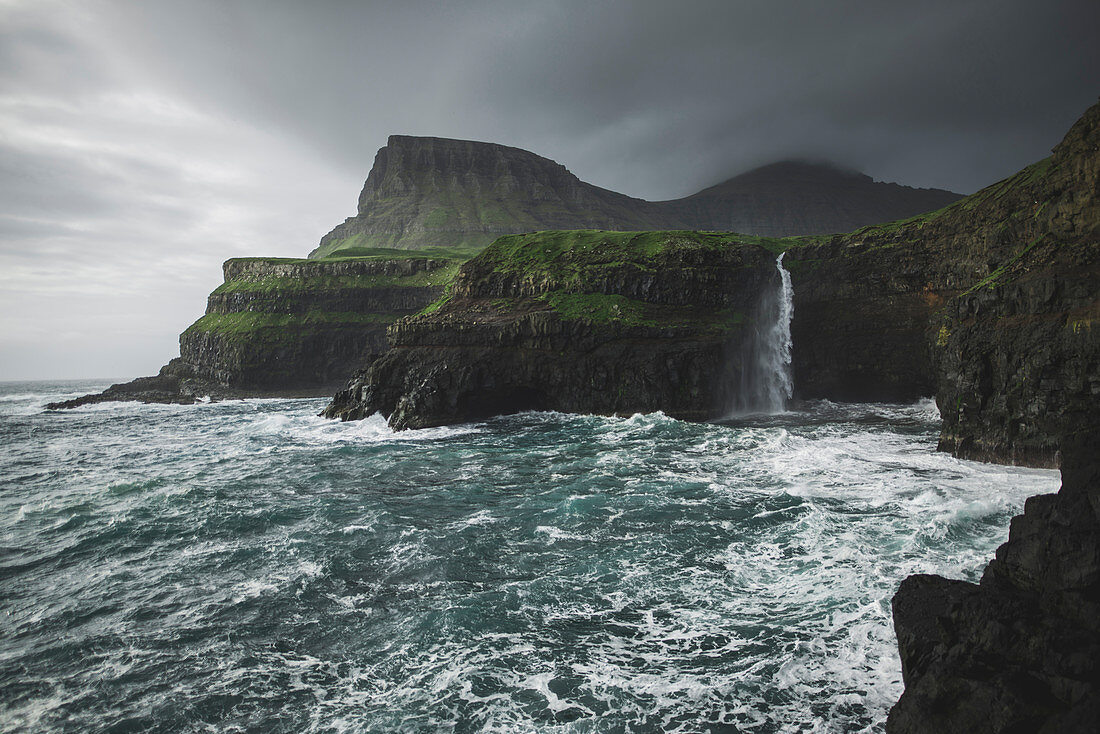 Denmark,Faroe Islands,Gasadalur Village,M?Lafossur Waterfall,Coastline with Mulafossur Waterfall falling into Atlantic Ocean in stormy day