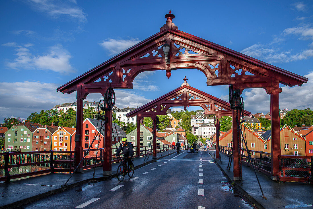 Fahrradfahrer auf der Brücke Bybrua am Fluss Nidelv mit alten Lagerhäusern, Trondheim, Norwegen