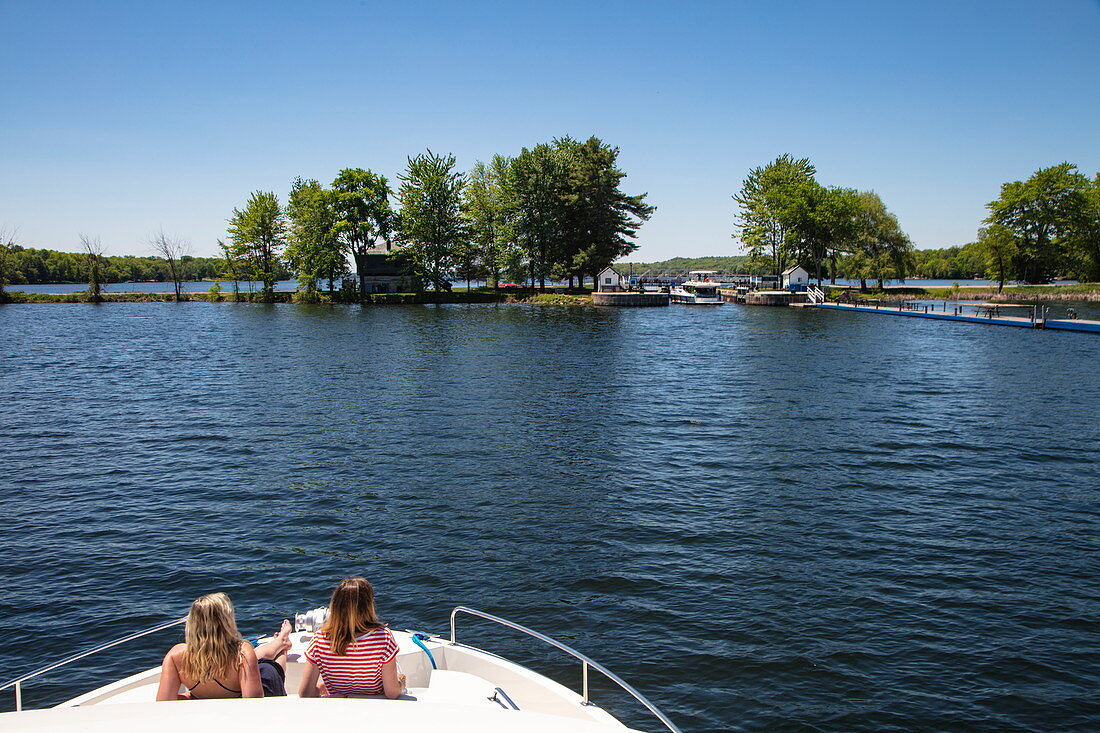 Two young women relax on the bow of a Le Boat Horizon houseboat as it approaches the lock at Narrows Lockstation, Lower Rideau Lake, Ontario, Canada, North America