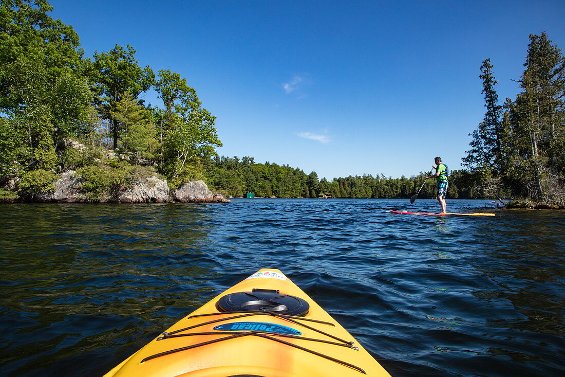 Tip of a yellow kayak and man on SUP stand-up paddleboard on Indian Lake, near Chaffey's Lock, Ontario, Canada, North America