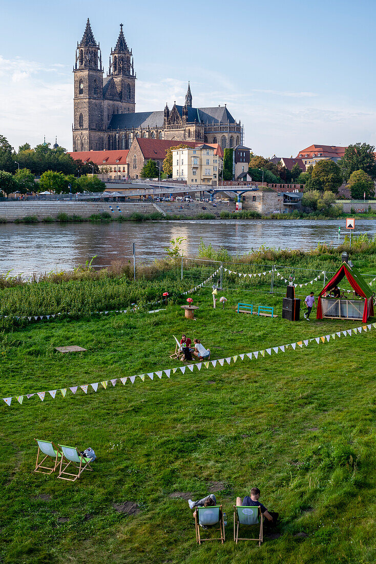 Young people sit on the Elbe in deck chairs, behind them Magdeburg Cathedral, Saxony-Anhalt, Germany