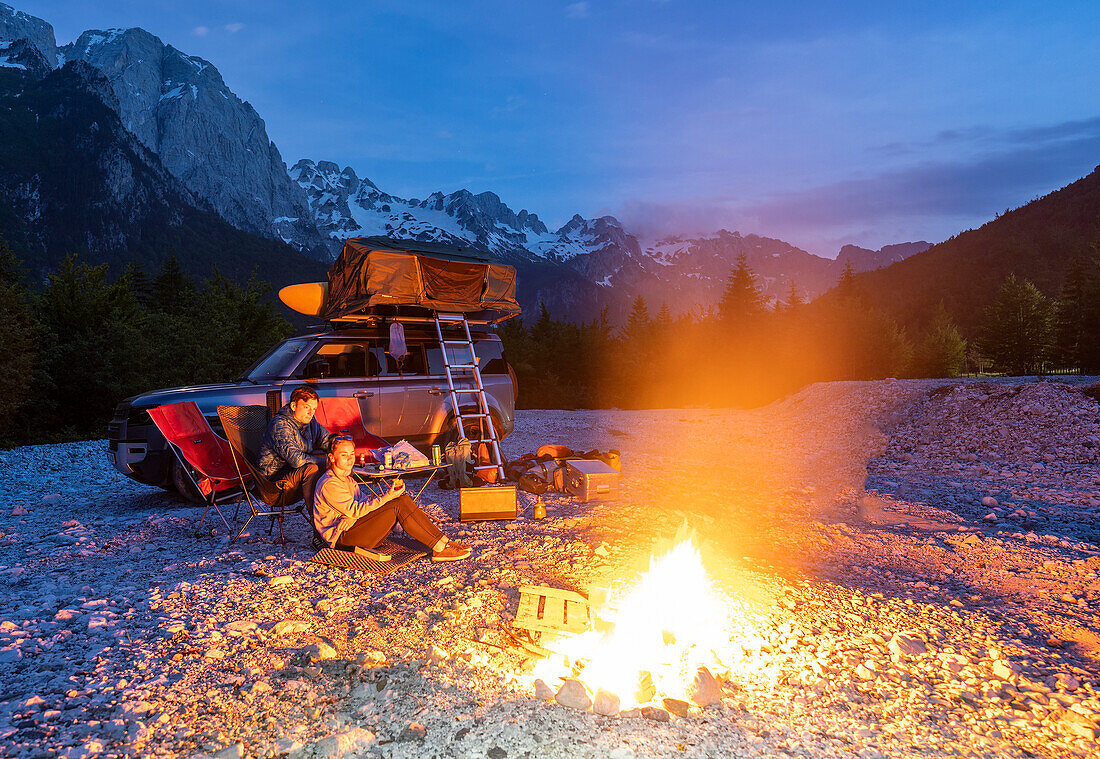 Albanien, Südeuropa, junges Paar vor Geländewagen mit Dachzelt, Lagerfeuer am Abend, Albanische Alpen, Valbona