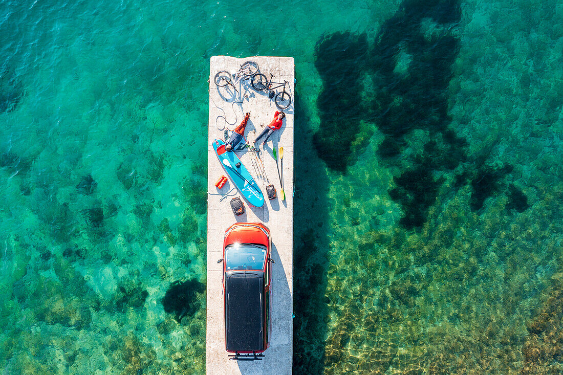 Roadtrip Kroatien, zwei Menschen mit Freizeit Equipment, Fahrräder, SUP Board und Campingbus auf einem Steg