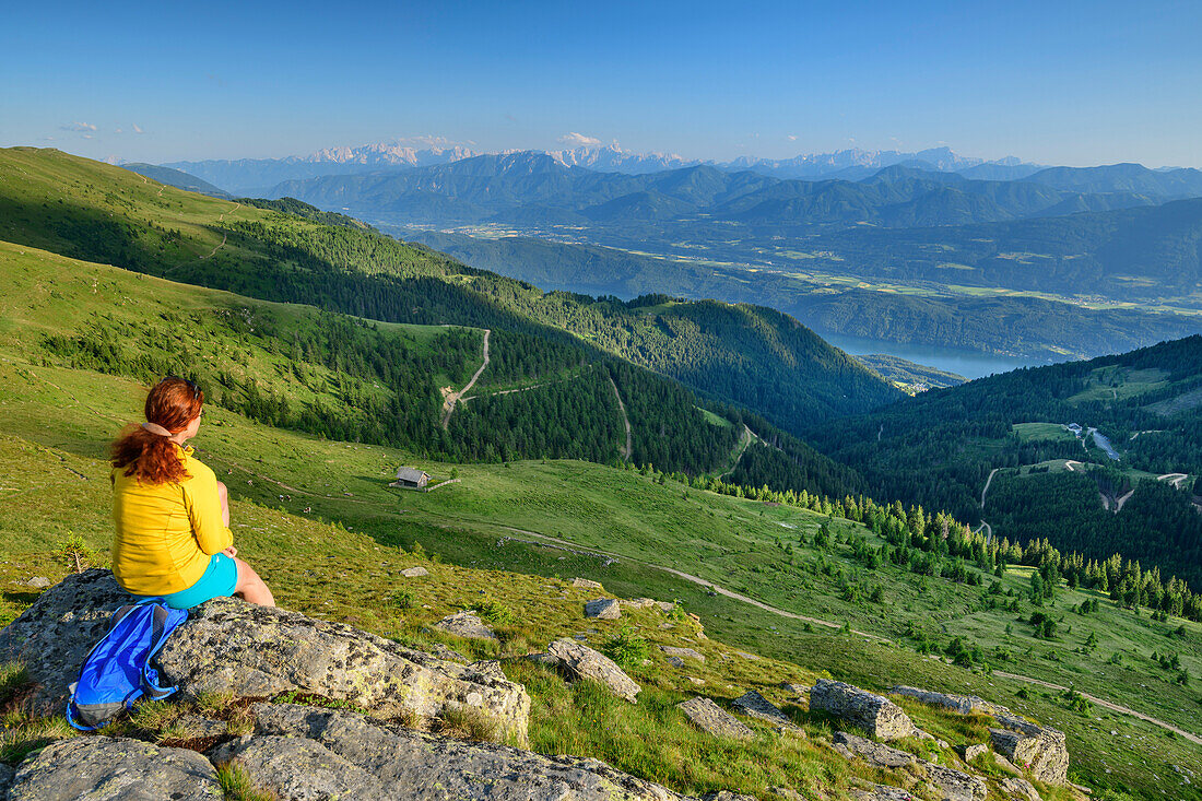 Frau beim Wandern sitzt auf Felsen und blickt ins Tal, Kamplnock, Nockberge, Nockberge-Trail, UNESCO Biosphärenpark Nockberge, Gurktaler Alpen, Kärnten, Österreich