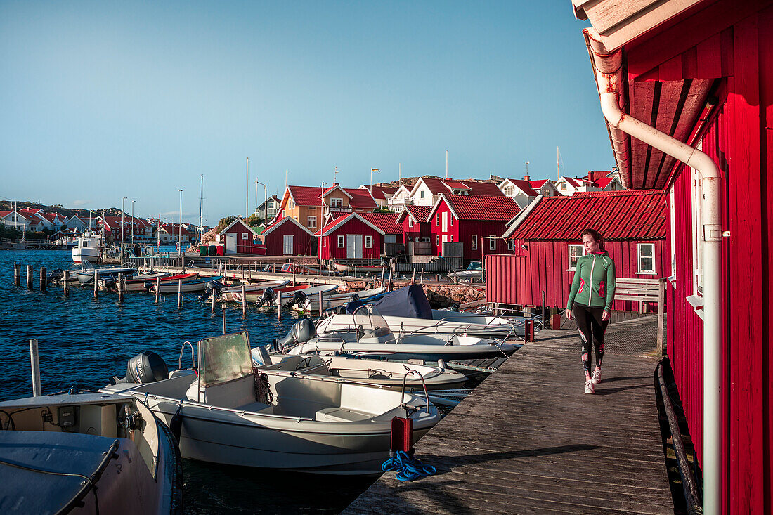 Frau am Hafen im Dorf Kyrkesund auf der Schäreninsel Tjörn an der Westküste von Schweden, blauer Himmel mit Sonne\n