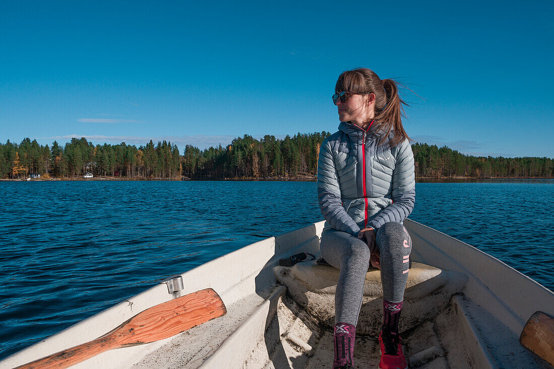 Woman sitting in paddle boat on lake in Lapland with sun and blue sky