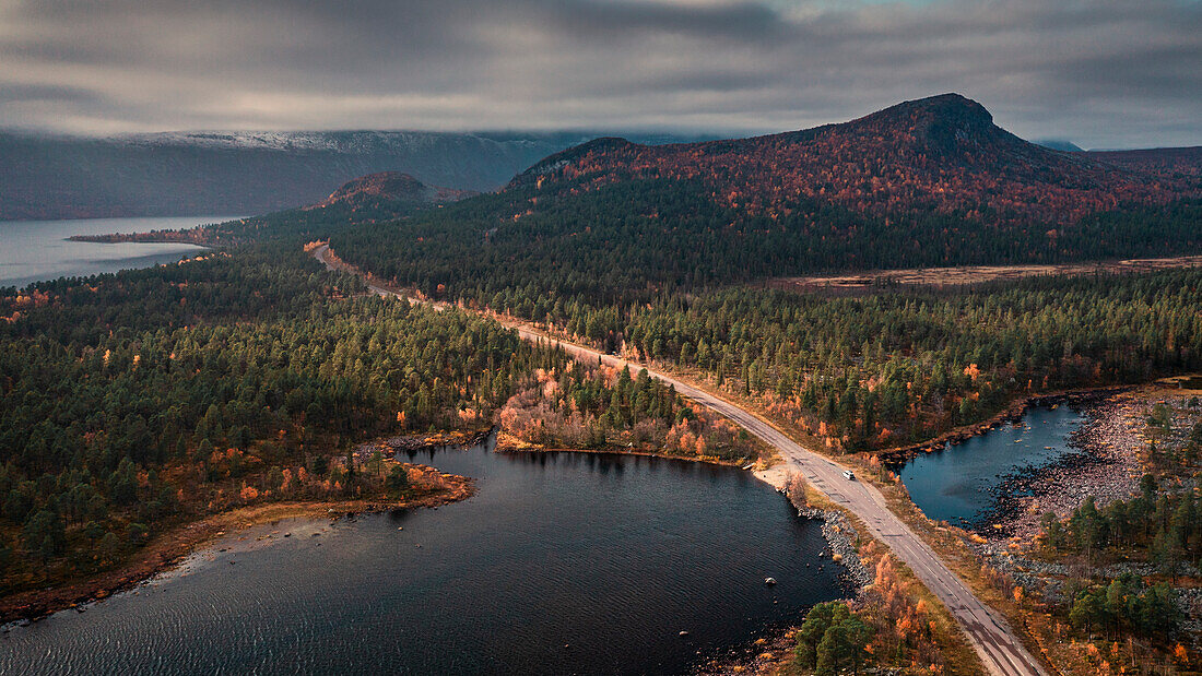 Road through landscape with lake and mountains in Stora Sjöfallet National Park in autumn in Lapland in Sweden from above