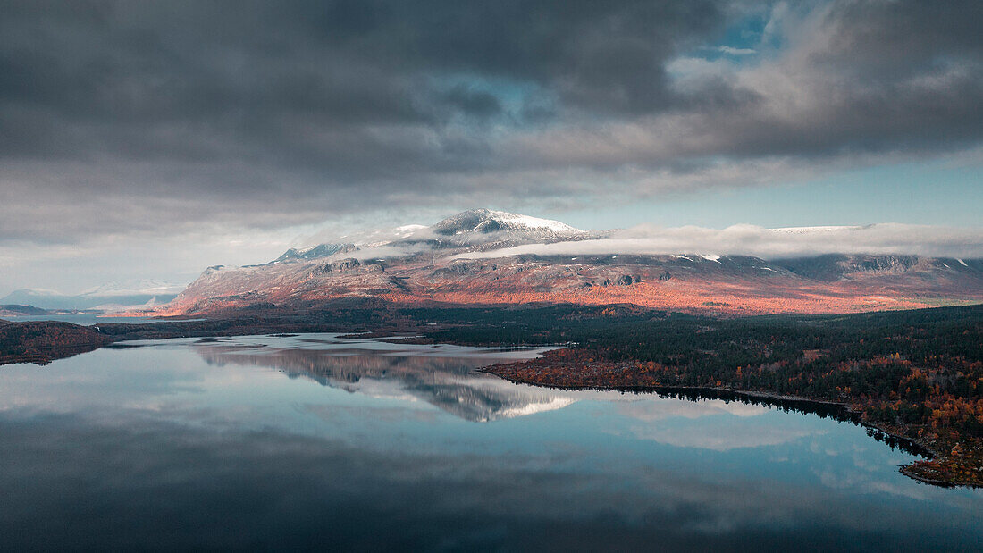 Landscape with snowy mountains and reflection in the lake in Stora Sjöfallet National Park in autumn in Lapland in Sweden from above