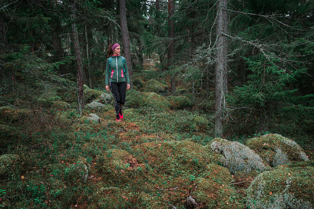 Woman hiking through forest with moss covered ground in Tyresta National Park in Sweden