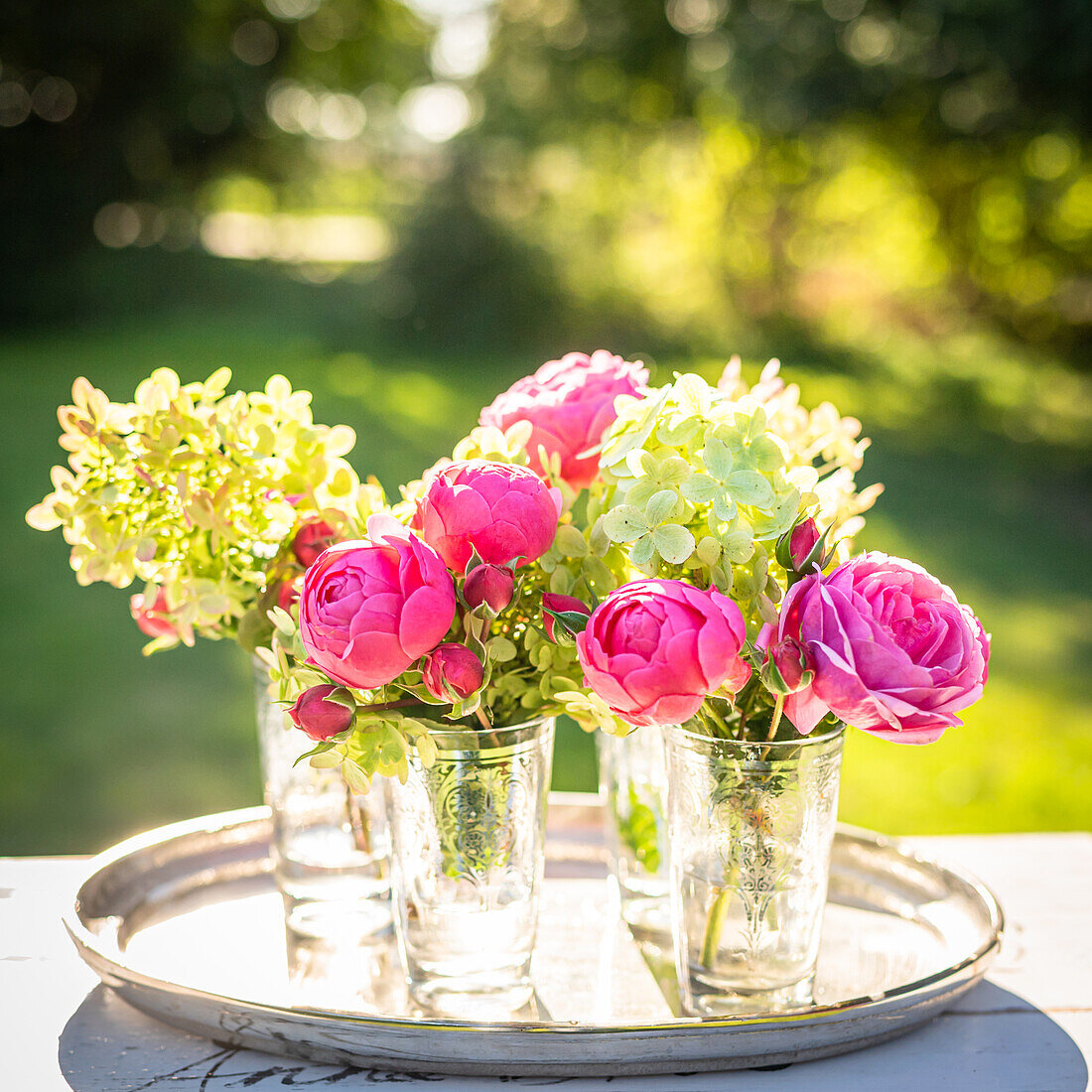 Rosa Rosen und weiße Hortensien in Vasen auf Tablett im Freien