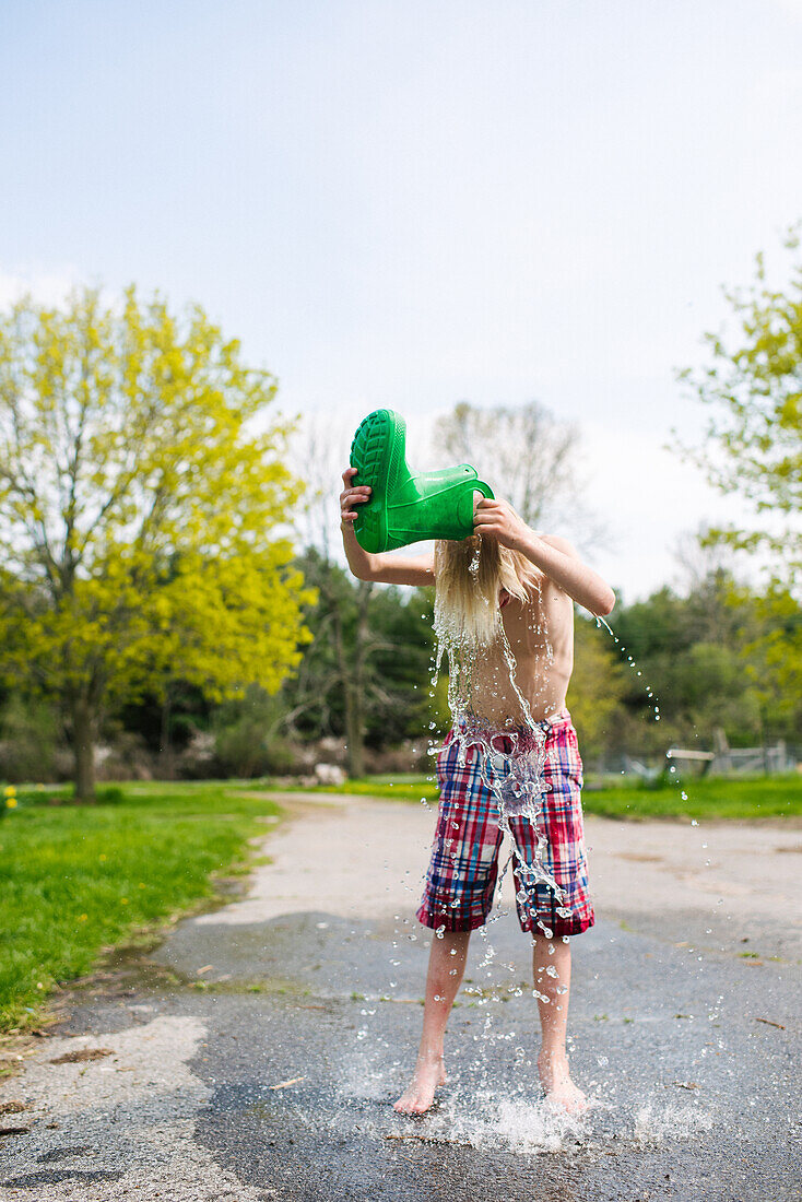Kanada, Kingston, Junge mit freiem Oberkörper (8-9) gießt Wasser aus Gummistiefel auf den Kopf