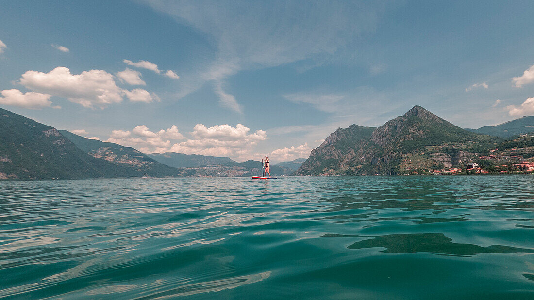 Frau paddelt auf SUP Board vor Bergen im Iseosee in Italien