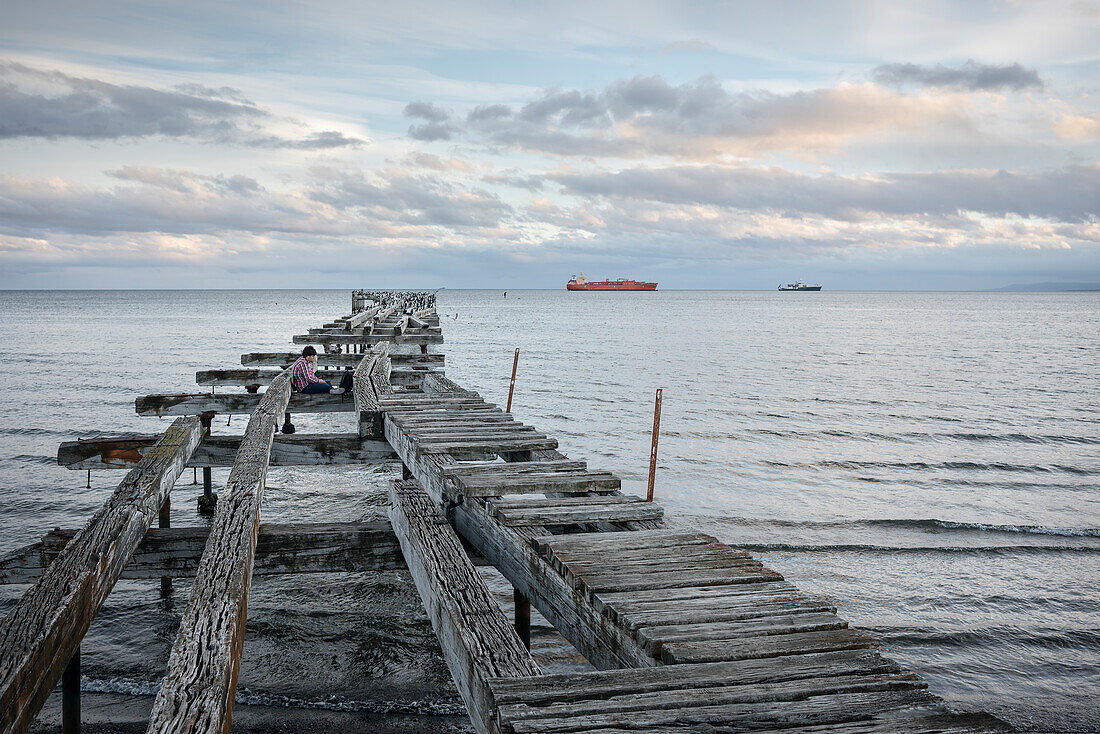 Young man sitting on jetty at Playa Norte, Punta Arenas, Patagonia, Chile, South America