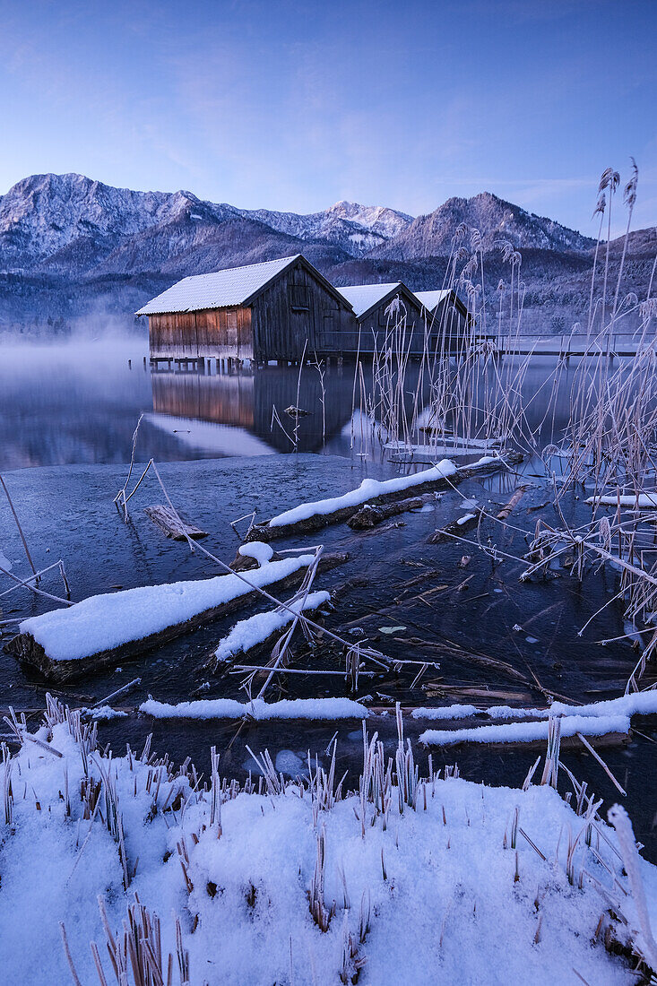 Holzhütten und Steg am Kochelsee zur blauen Stunde im Winter, im Vordergrund das vereiste Seeufer, Schlehdorf, Bayern, Deutschland, Europa
