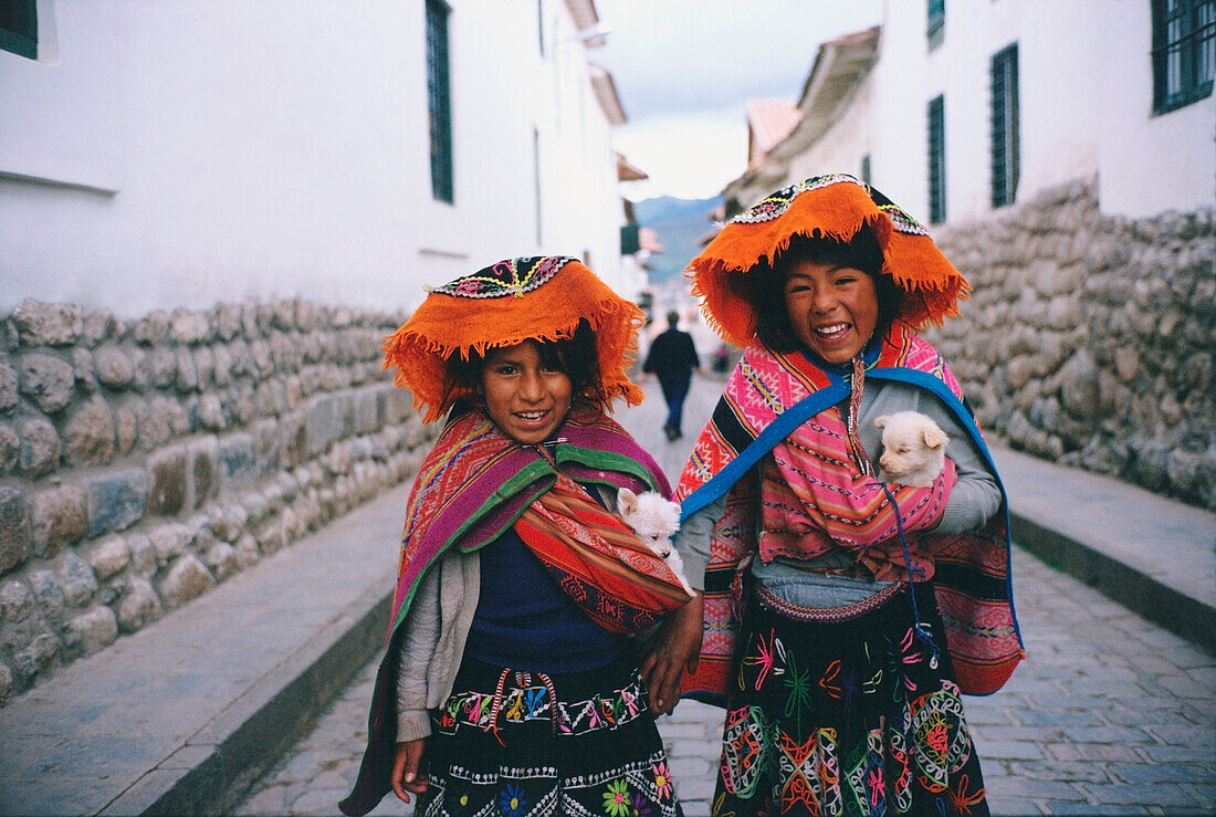 Two girls standing in the street holding two puppies, Cuzco, Cusco Region, Peru