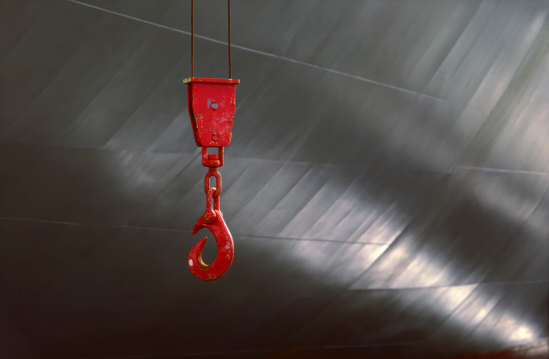 Large red winch hook against side of ship and reflections from water