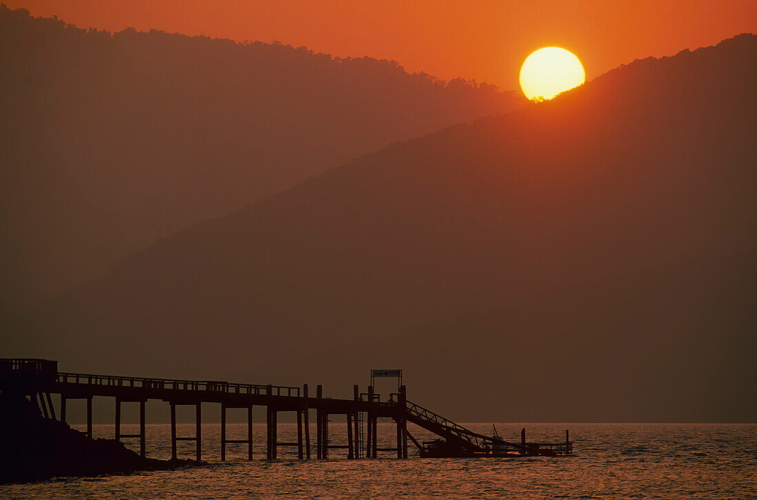 Sun setting behind the hills and Jetty on water