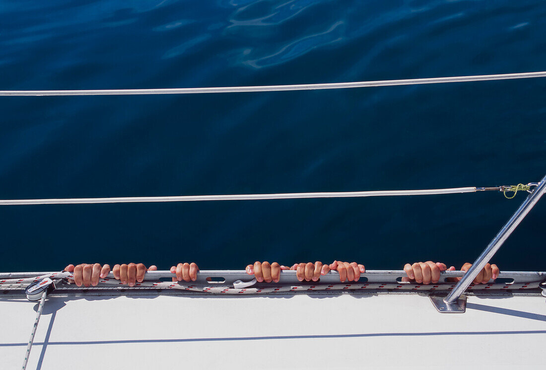 Vier Fingerpaare hängen in ruhigem Wasser an der Seite der Yacht