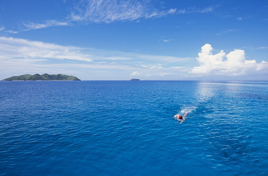 Mann schwimmt im tropischen Wasser mit Insel im Hintergrund