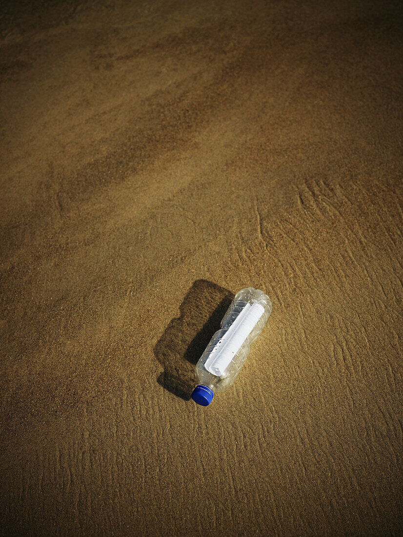 Plastiktrinkflasche mit Nachricht, die auf Sand ruht