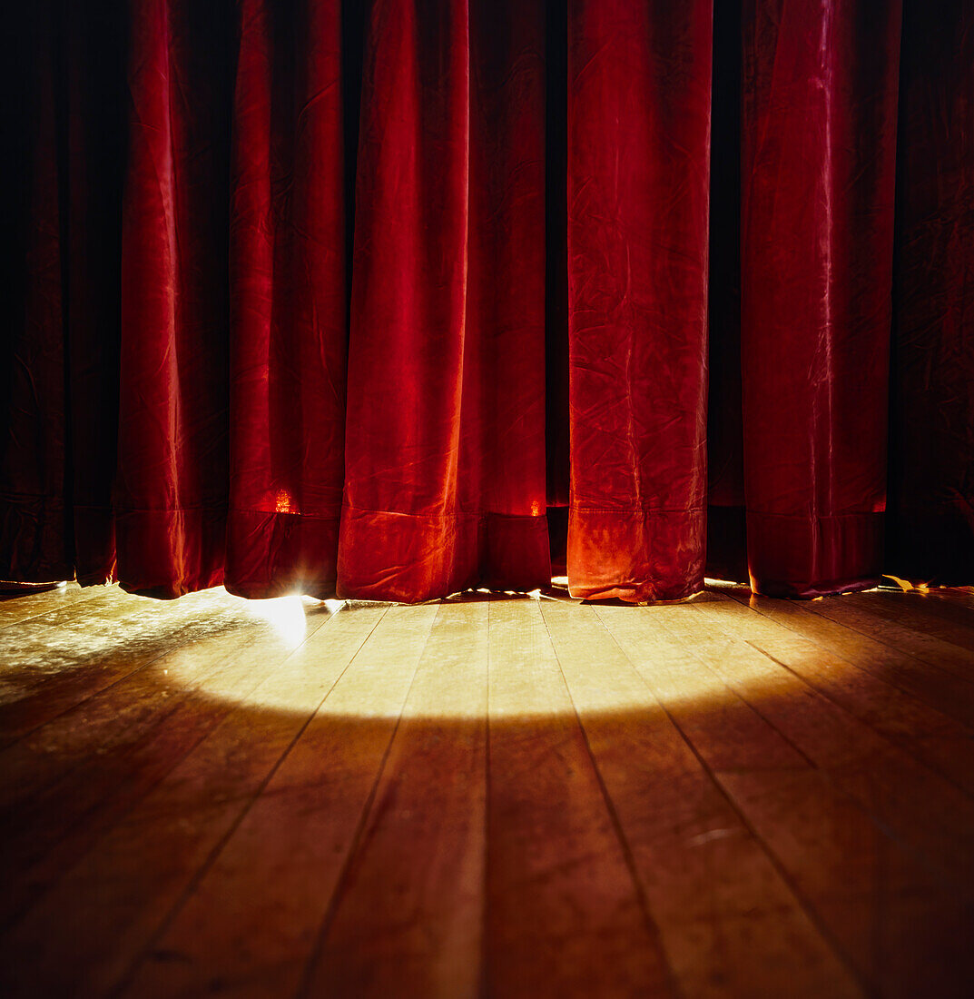 Spotlight shining on red stage curtains and wooden floor