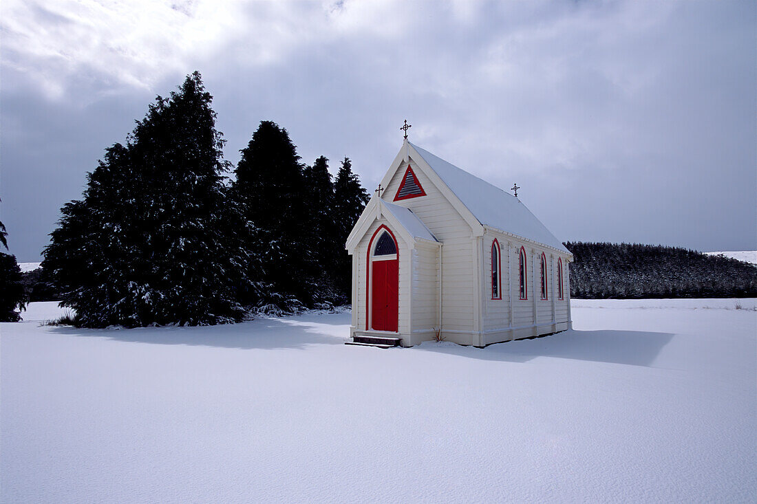 Alte Holzkirche mit roter Tür unter verschneiter Landschaft
